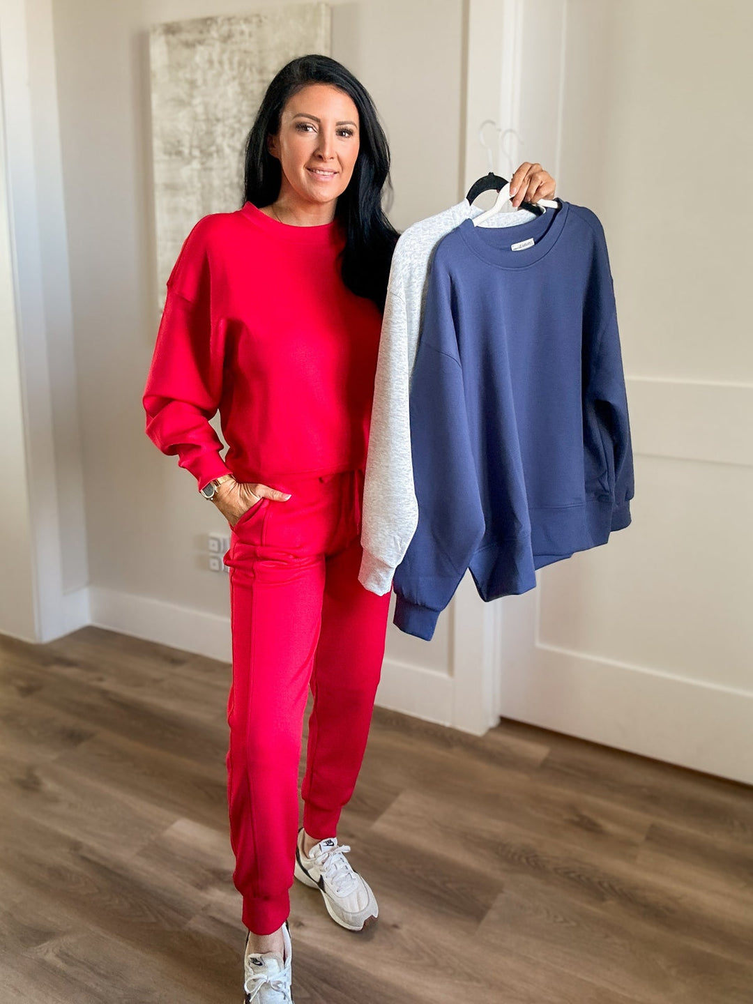 Woman in red outfit holding a blue and white sweater in a room with wooden floor and white walls.