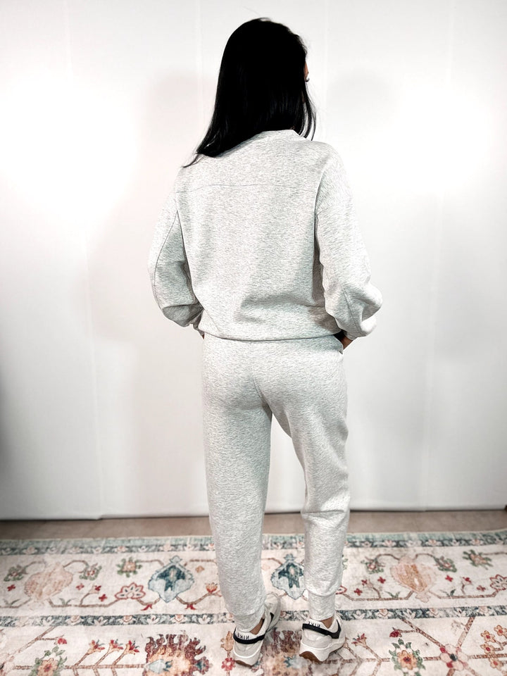 Person wearing a gray tracksuit standing on a patterned rug with a white wall background