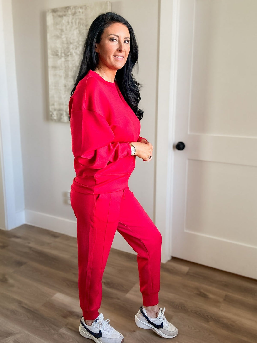 Woman in a red outfit standing in a room with wooden flooring and white walls.