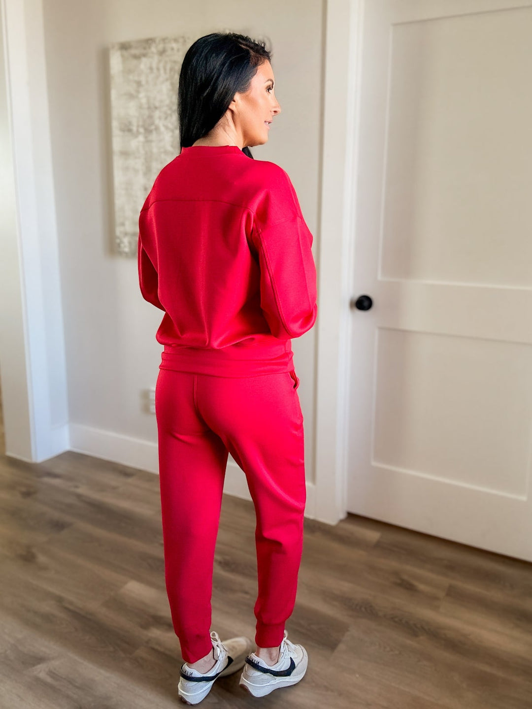 Person wearing a red tracksuit standing in a room with wooden flooring and a white door.