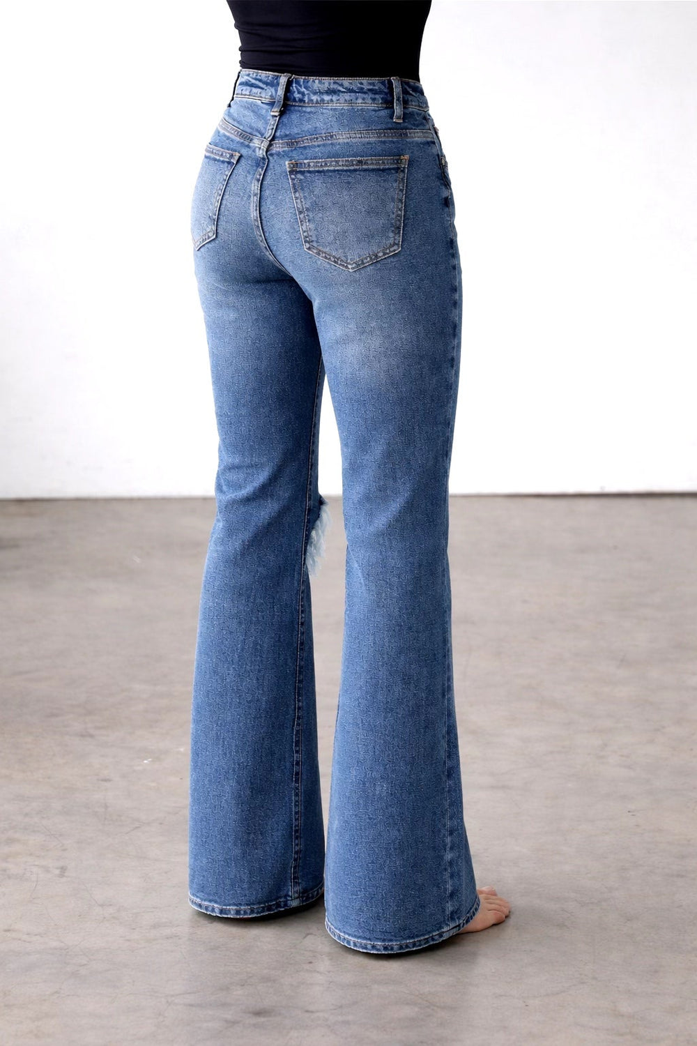 Blue flared jeans worn by a person on a plain background